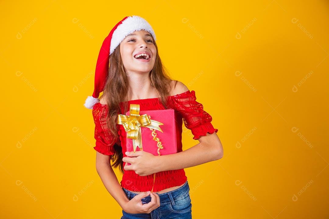 linda garota alegre com um chapéu de Natal em um fundo colorido segurando um presente