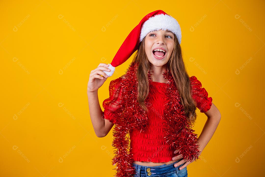 menina vestida para o natal encantada segurando o pompom do chapéu