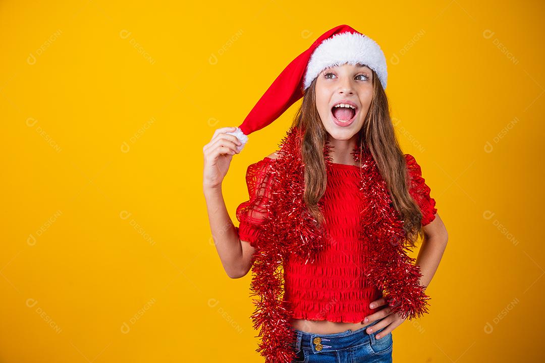 menina vestida para o natal encantada segurando o pompom do chapéu