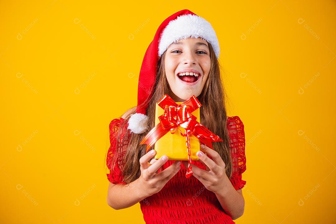 linda garota alegre com um chapéu de Natal em um fundo colorido segurando um presente