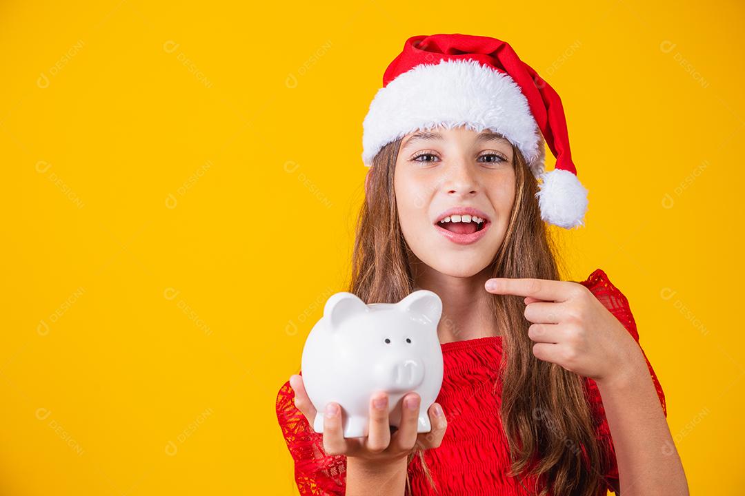 Menina sorridente com chapéu de natal segurando o cofrinho