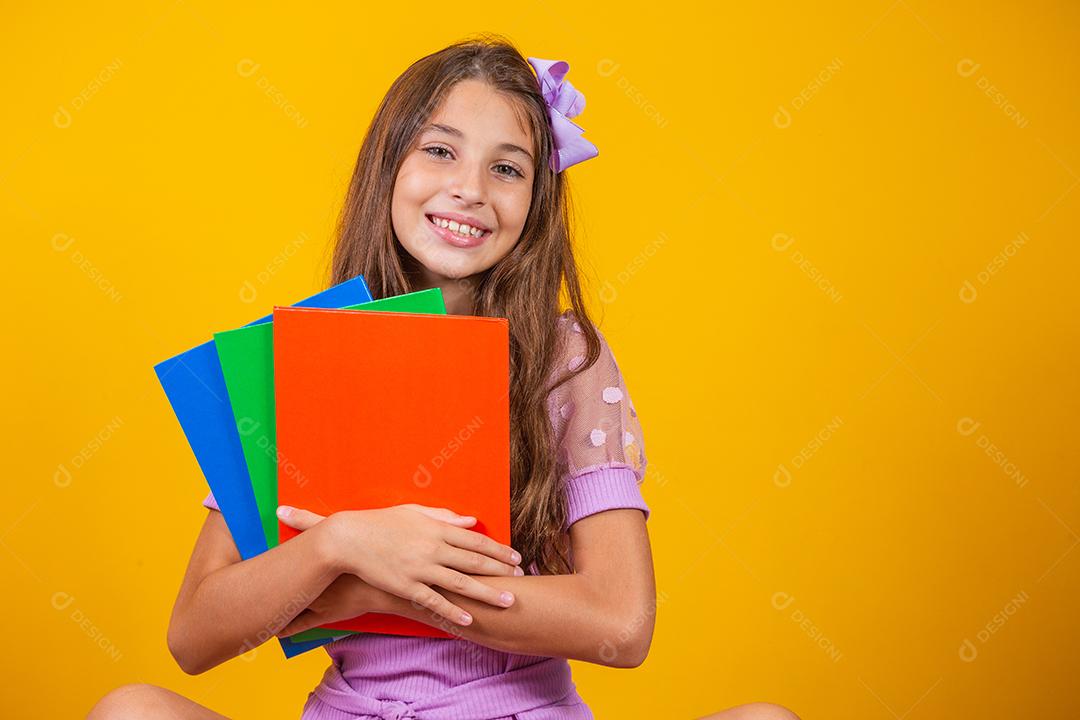 Linda garota sorridente segurando livros indo para a escola. feche o retrato, fundo amarelo isolado