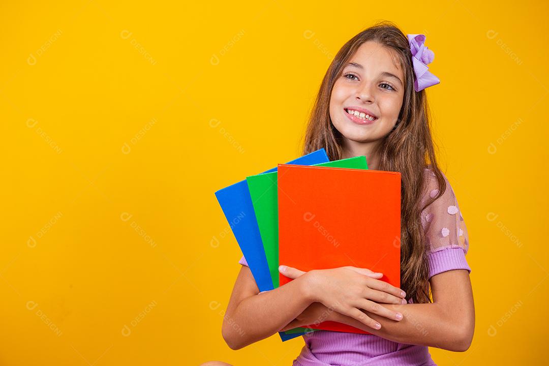 Linda garota sorridente segurando livros indo para a escola. feche o retrato, fundo amarelo isolado