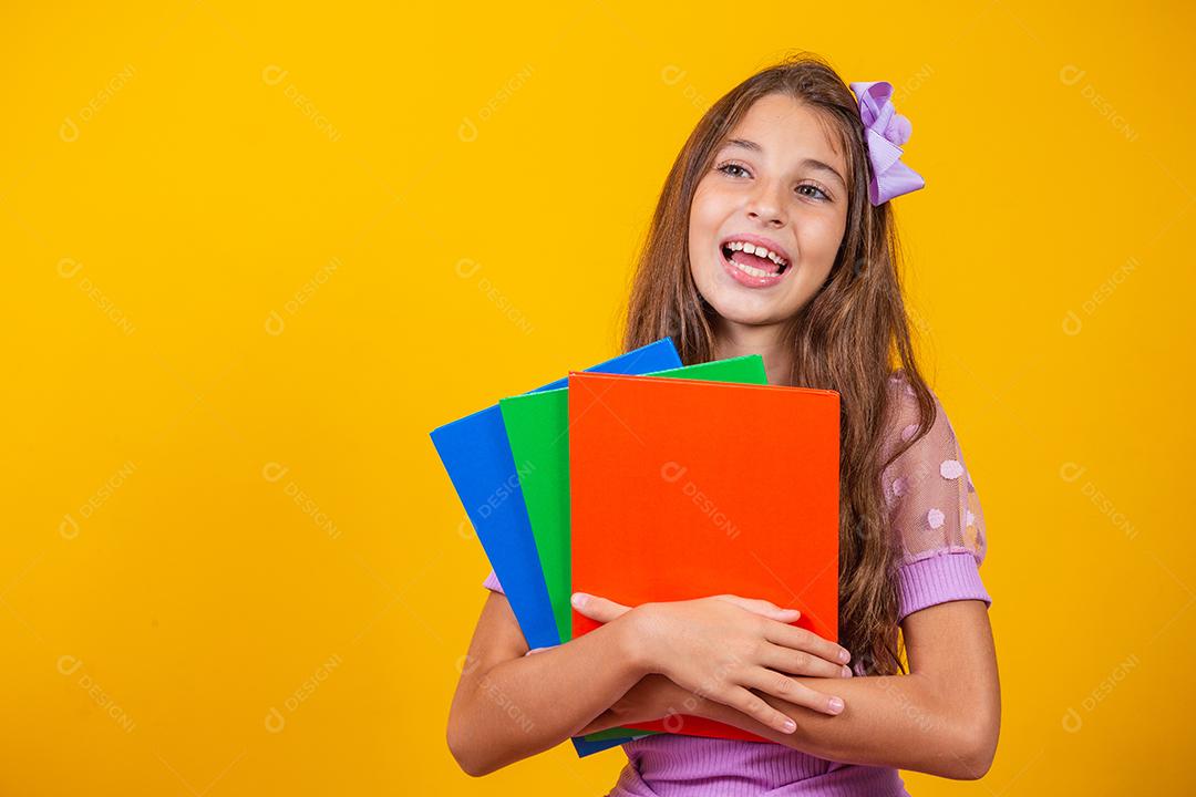 Linda garota sorridente segurando livros indo para a escola. feche o retrato, fundo amarelo isolado