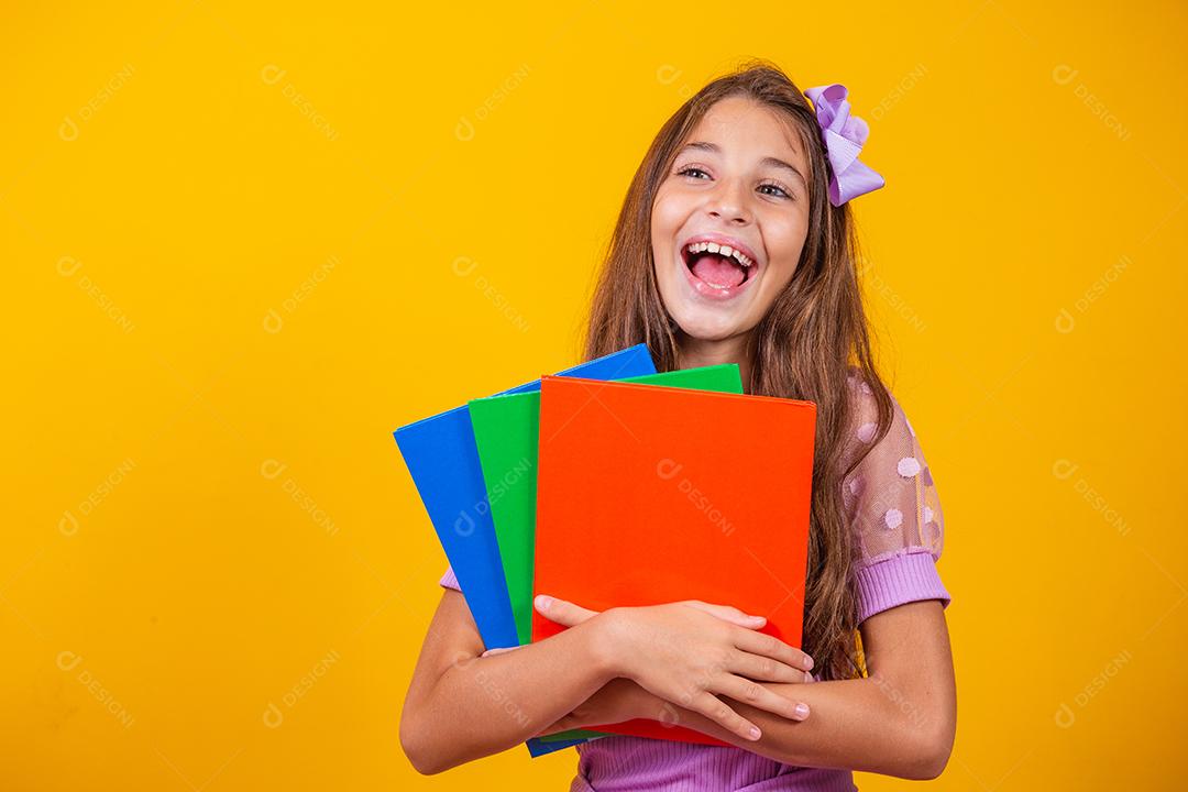 Linda garota sorridente segurando livros indo para a escola. feche o retrato, fundo amarelo isolado