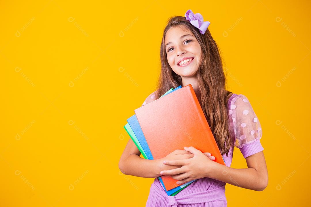 Linda garota sorridente segurando livros indo para a escola. feche o retrato, fundo amarelo isolado