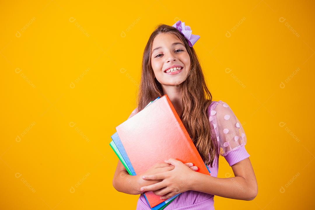 Linda garota sorridente segurando livros indo para a escola. feche o retrato, fundo amarelo isolado