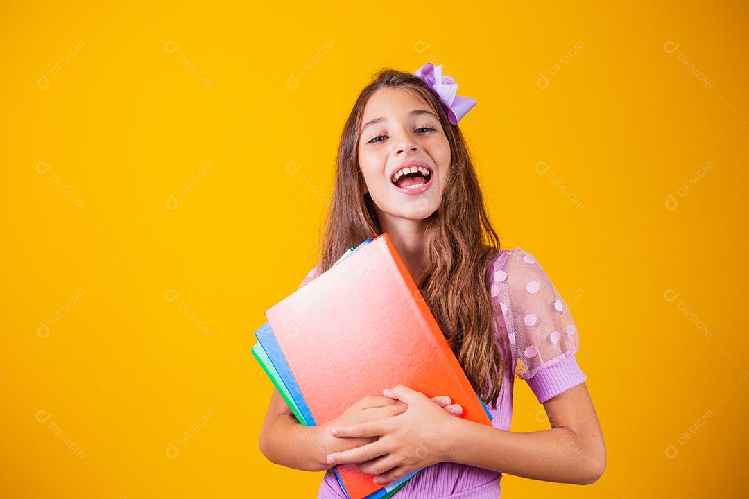 Linda garota sorridente segurando livros indo para a escola. feche o retrato, fundo amarelo isolado