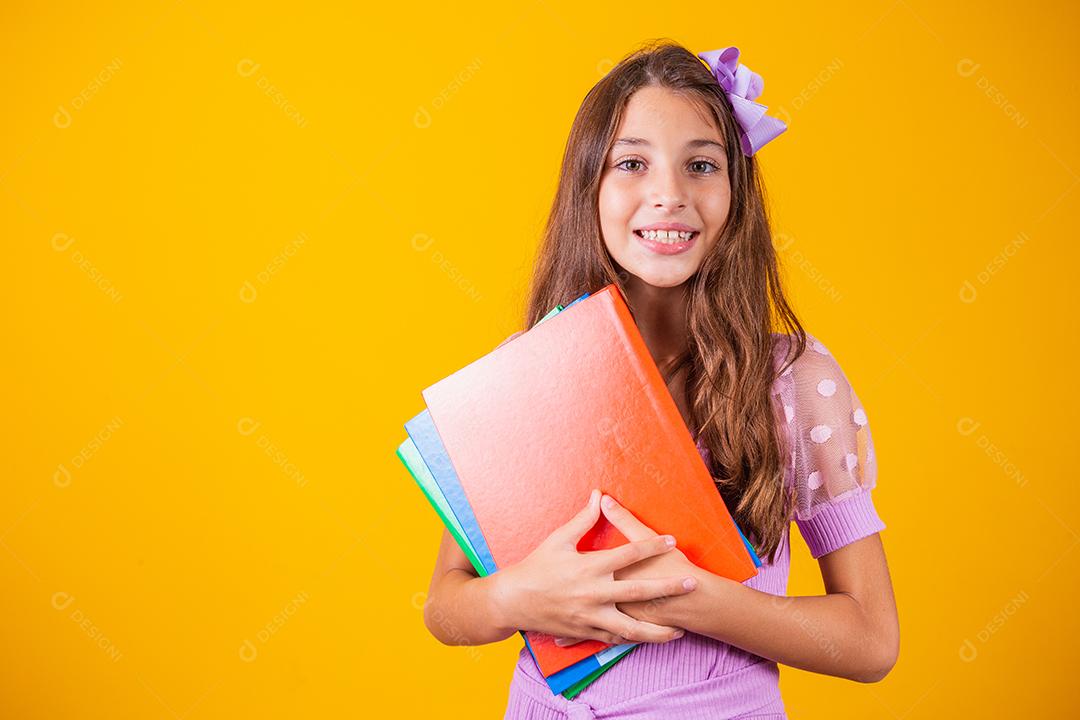 Linda garota sorridente segurando livros indo para a escola. feche o retrato, fundo amarelo isolado
