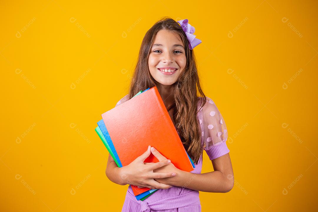 Linda garota sorridente segurando livros indo para a escola. feche o retrato, fundo amarelo isolado