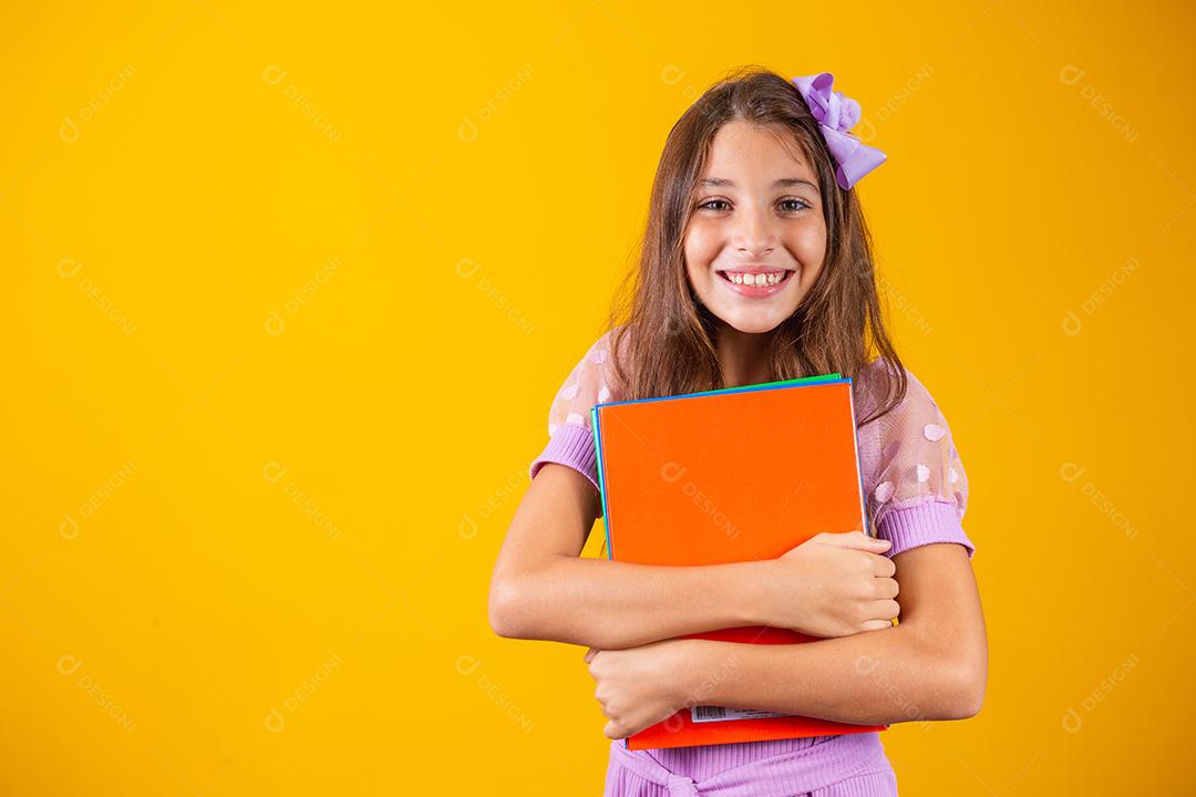 Linda garota sorridente segurando livros indo para a escola. feche o retrato, fundo amarelo isolado