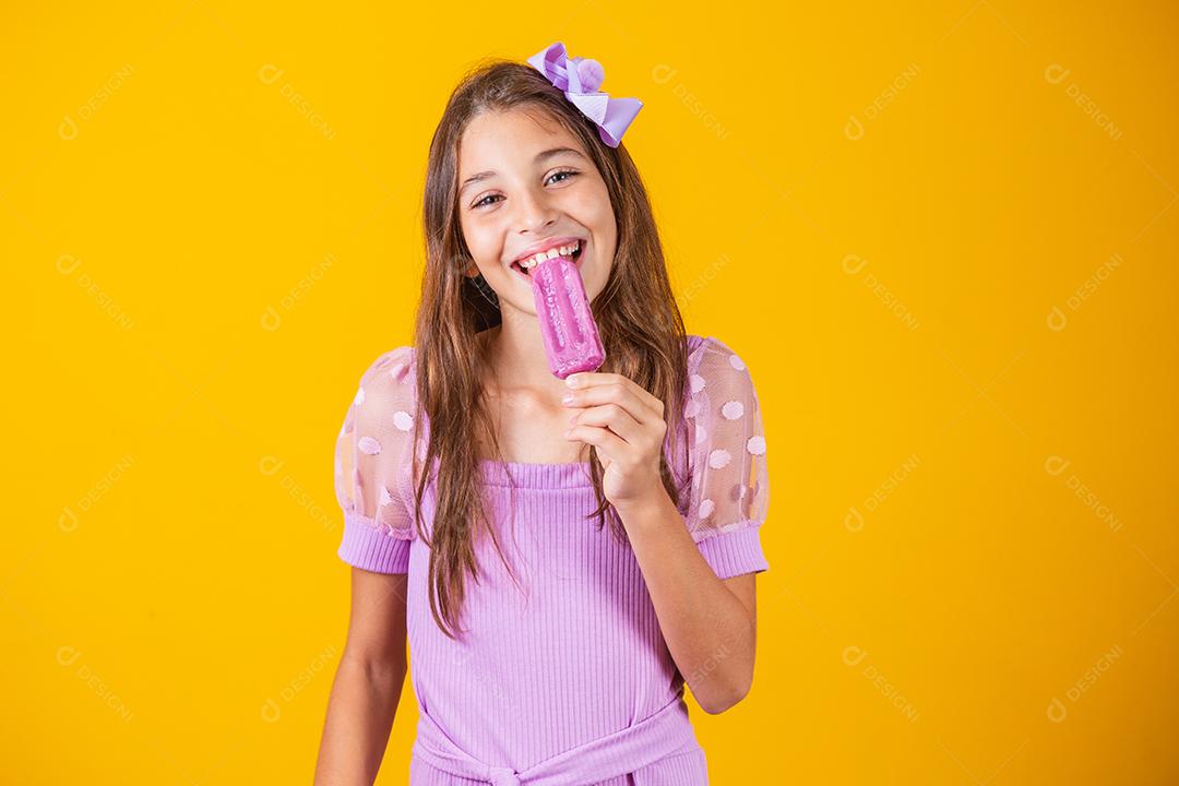 menina comendo um picolé congelado. Adorável menina com delicioso sorvete contra fundo de cor