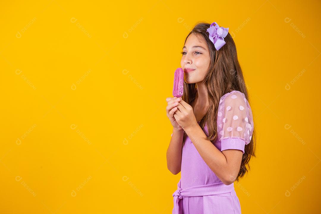 Menina comendo um picolé colorido congelado no verão. Garota segurando um picolé