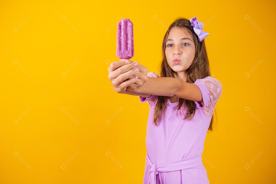 Menina comendo um picolé colorido congelado no verão. Garota segurando um picolé