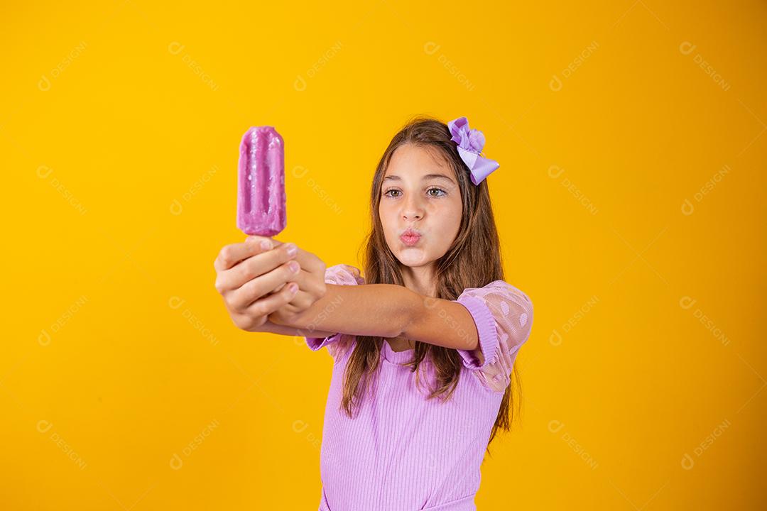 Menina comendo um picolé colorido congelado no verão. Garota segurando um picolé