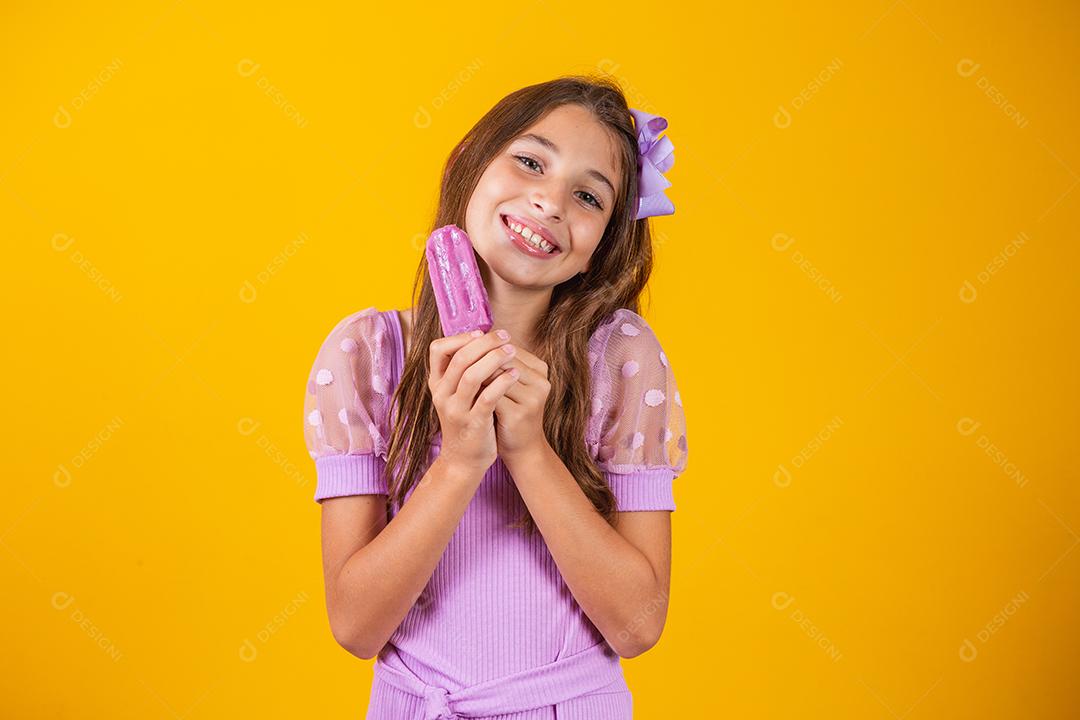 Menina comendo um picolé colorido congelado no verão. Garota segurando um picolé