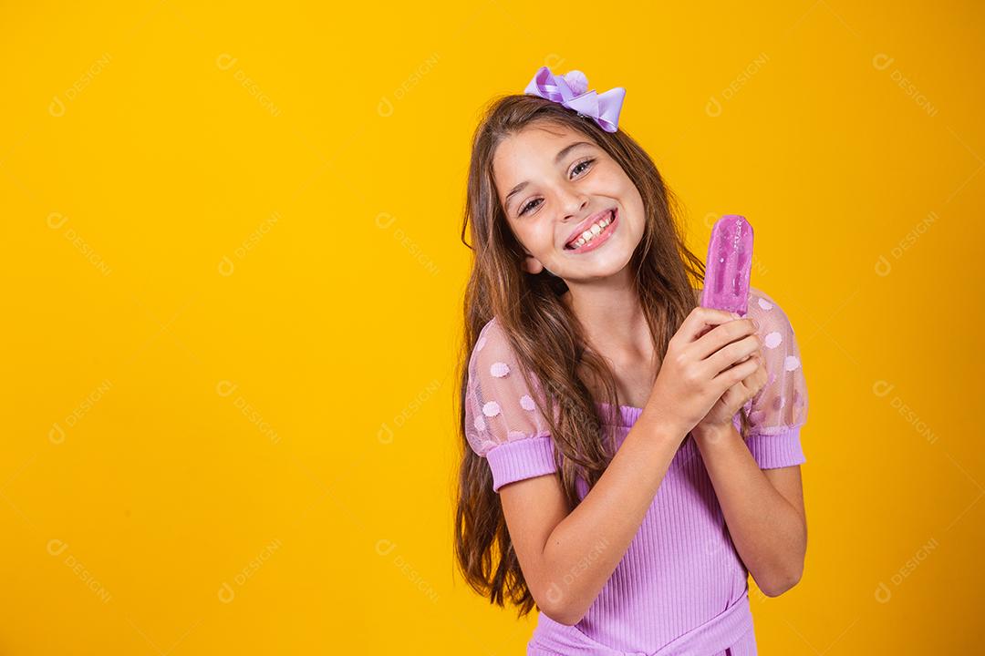 Menina comendo um picolé colorido congelado no verão. Garota segurando um picolé