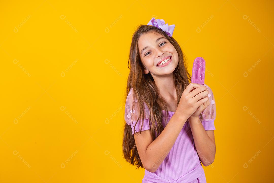 pequena garota caucasiana com delicioso picolé de uva sorrindo olhando para a câmera. Verão