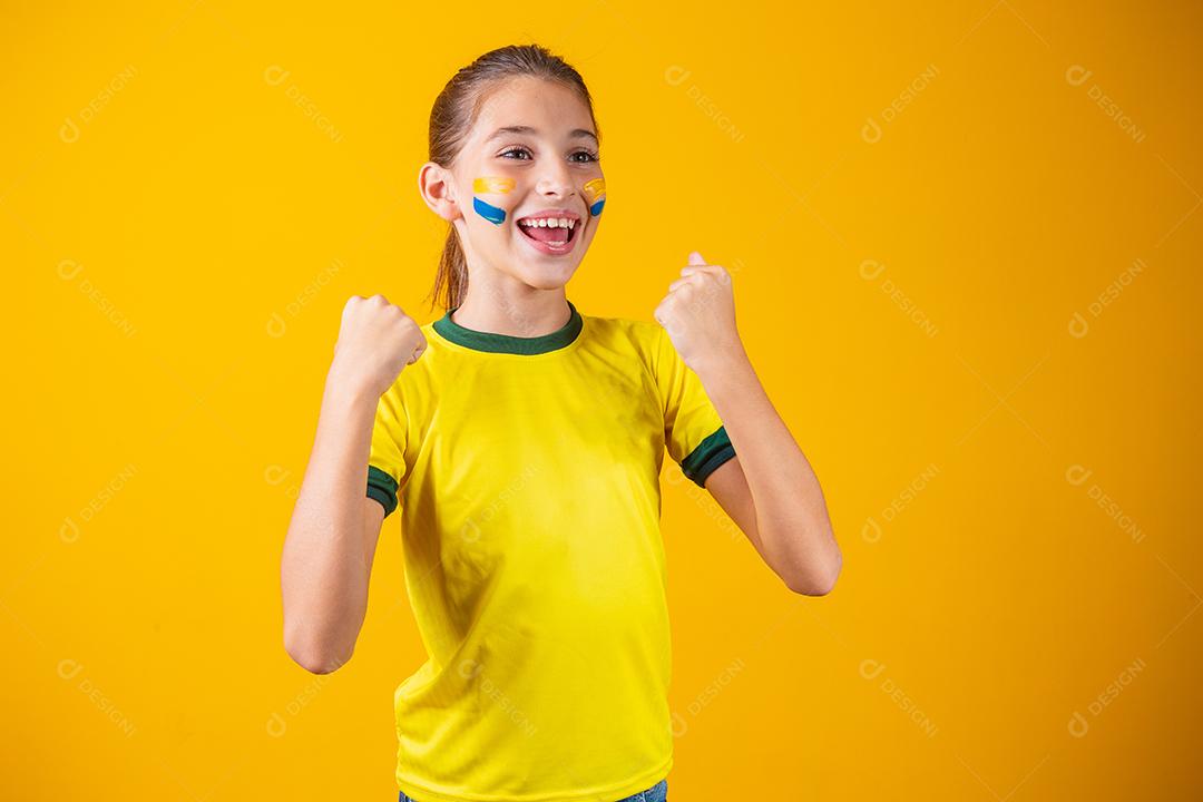 Linda garotinha torcendo por seu time em fundo amarelo. Menina comemorando o gol e comemorando a vitória do Brasil