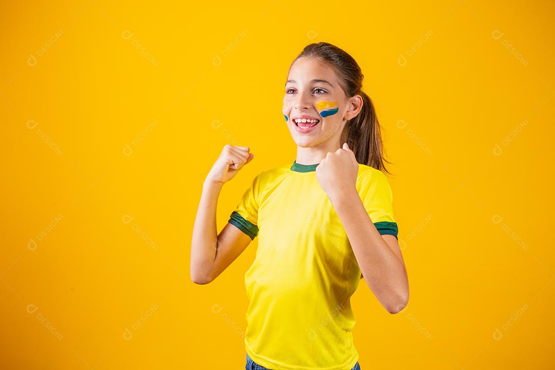 Linda garotinha torcendo por seu time em fundo amarelo. Menina comemorando o gol e comemorando a vitória do Brasil