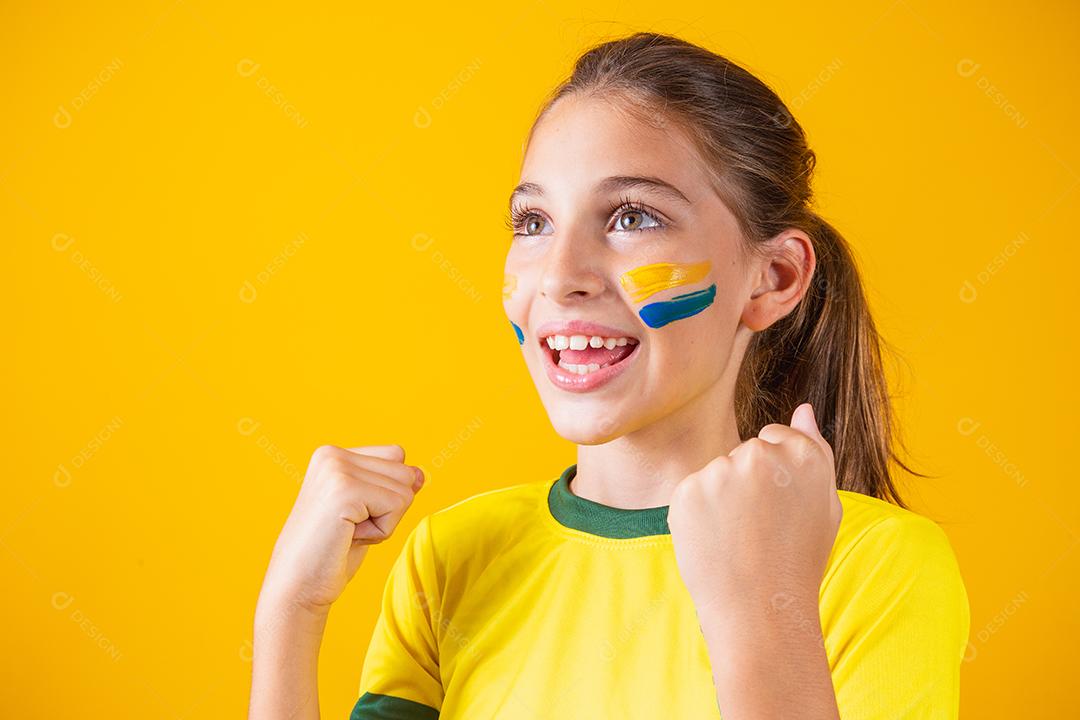 Linda garotinha torcendo por seu time em fundo amarelo. Menina comemorando o gol e comemorando a vitória do Brasil