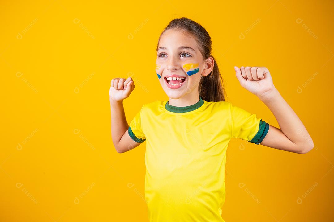 Linda garotinha torcendo por seu time em fundo amarelo. Menina comemorando o gol e comemorando a vitória do Brasil