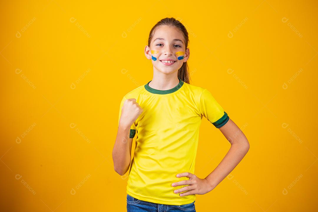 Linda garotinha torcendo por seu time em fundo amarelo. Menina comemorando o gol e comemorando a vitória do Brasil