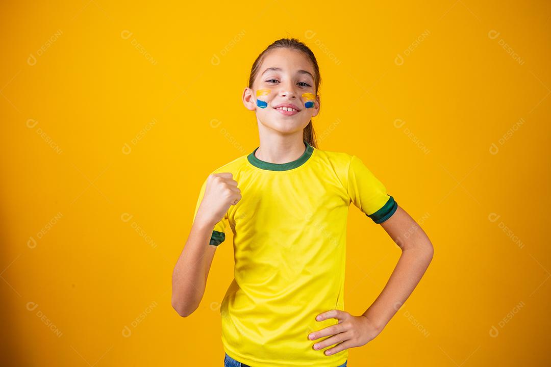 Linda garotinha torcendo por seu time em fundo amarelo. Menina comemorando o gol e comemorando a vitória do Brasil