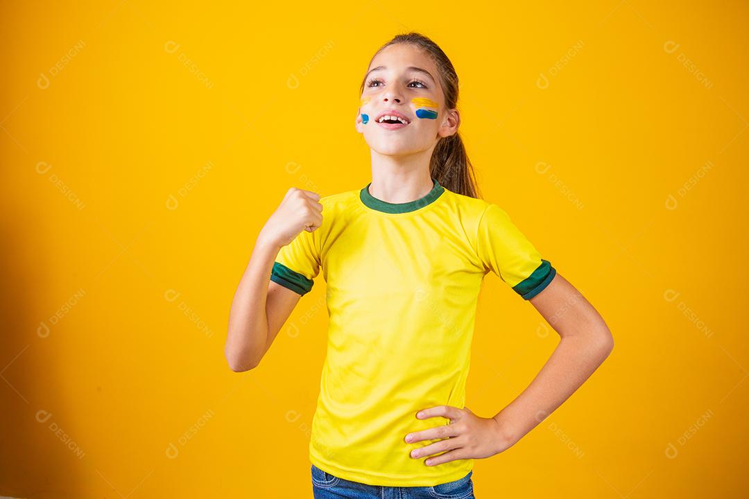 Linda garotinha torcendo por seu time em fundo amarelo. Menina comemorando o gol e comemorando a vitória do Brasil