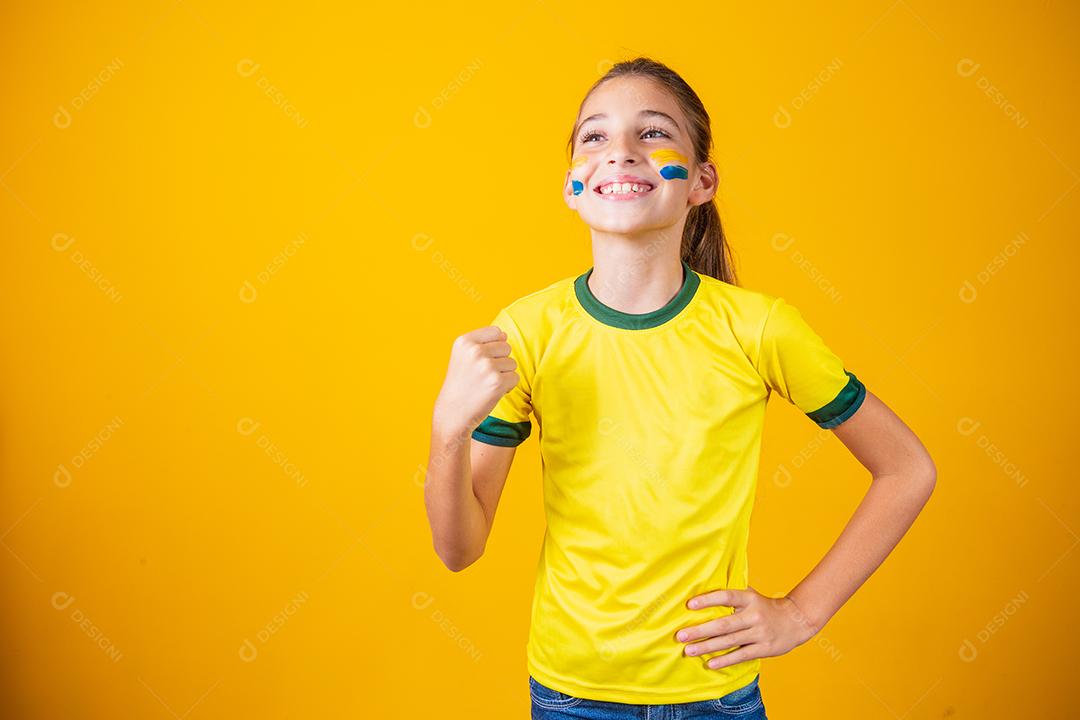Linda garotinha torcendo por seu time em fundo amarelo. Menina comemorando o gol e comemorando a vitória do Brasil