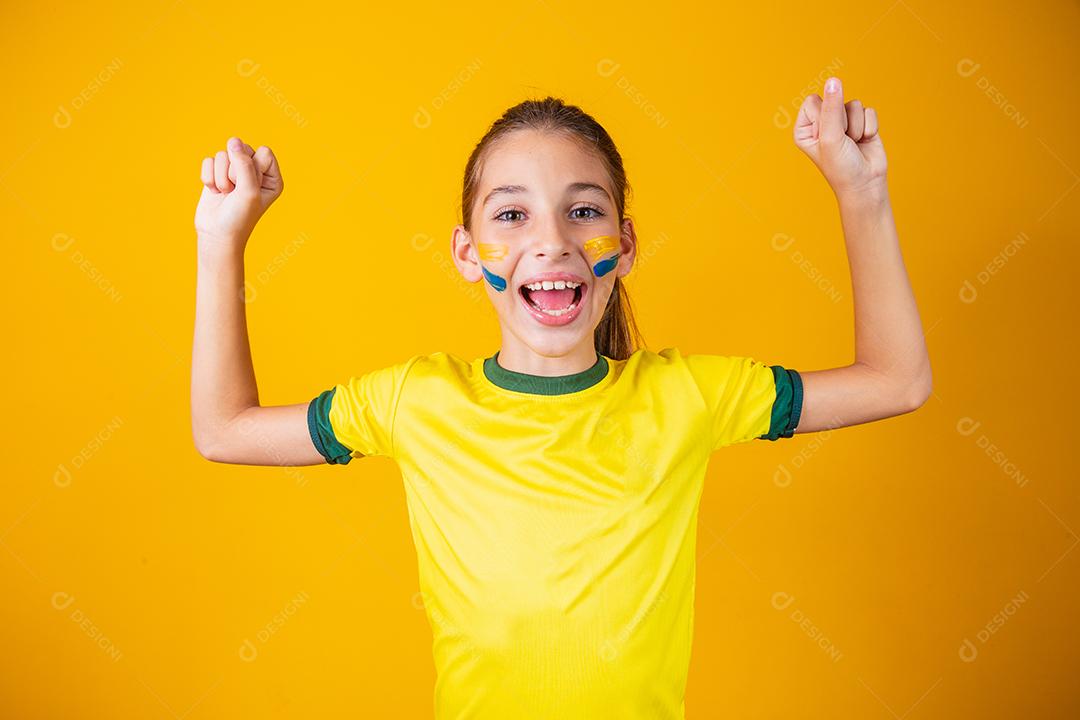 Linda garotinha torcendo por seu time em fundo amarelo. Menina comemorando o gol e comemorando a vitória do Brasil