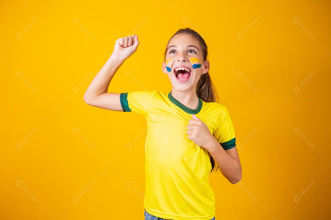 Linda garotinha torcendo por seu time em fundo amarelo. Menina comemorando o gol e comemorando a vitória do Brasil