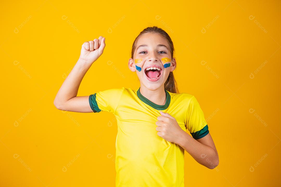 Linda garotinha torcendo por seu time em fundo amarelo. Menina comemorando o gol e comemorando a vitória do Brasil