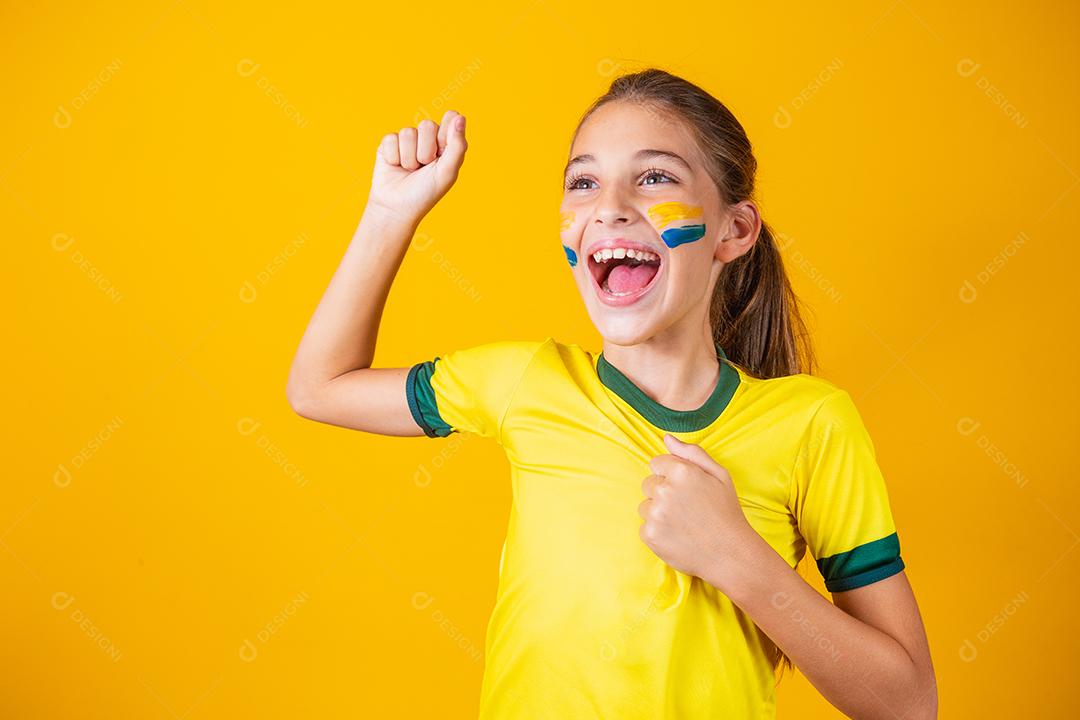 Linda garotinha torcendo por seu time em fundo amarelo. Menina comemorando o gol e comemorando a vitória do Brasil