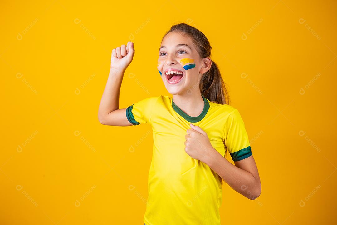 Linda garotinha torcendo por seu time em fundo amarelo. Menina comemorando o gol e comemorando a vitória do Brasil