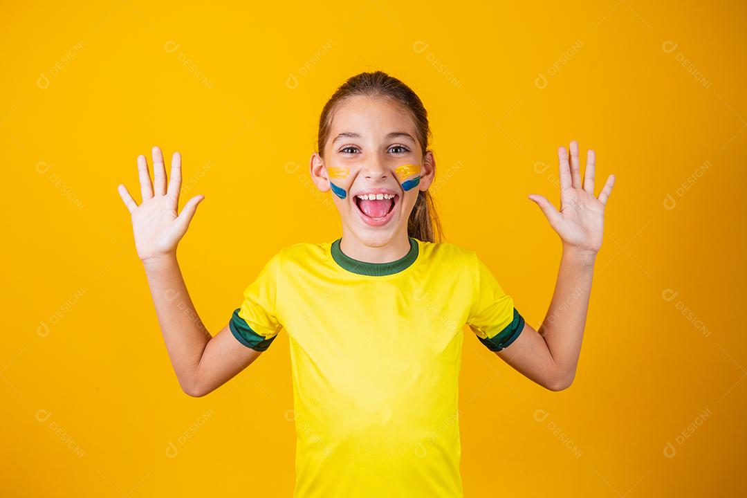 Linda garotinha entusiasmada e expressiva em um fundo amarelo vestida para o jogo do Brasil