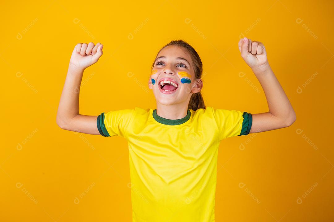 Linda garotinha torcendo por seu time em fundo amarelo. Menina comemorando o gol e comemorando a vitória do Brasil