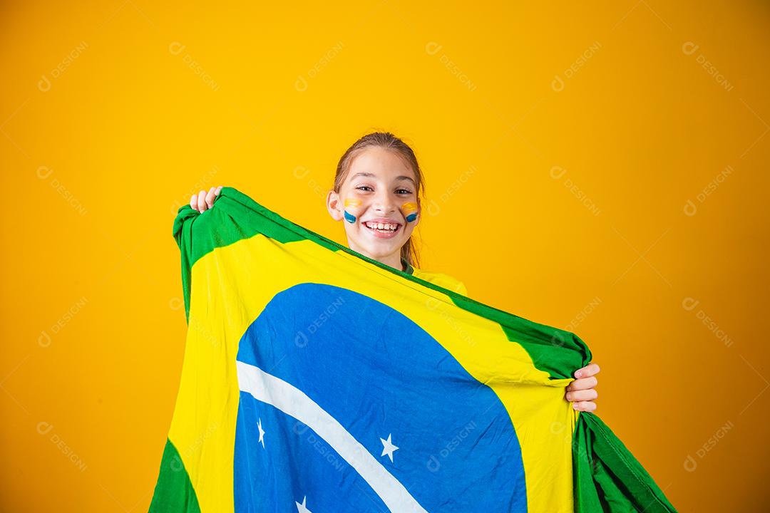 pequena garota caucasiana com bandeira do brasil em fundo amarelo. apoiador de criança brasileira