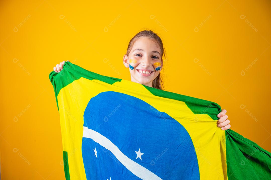 pequena garota caucasiana com bandeira do brasil em fundo amarelo. apoiador de criança brasileira