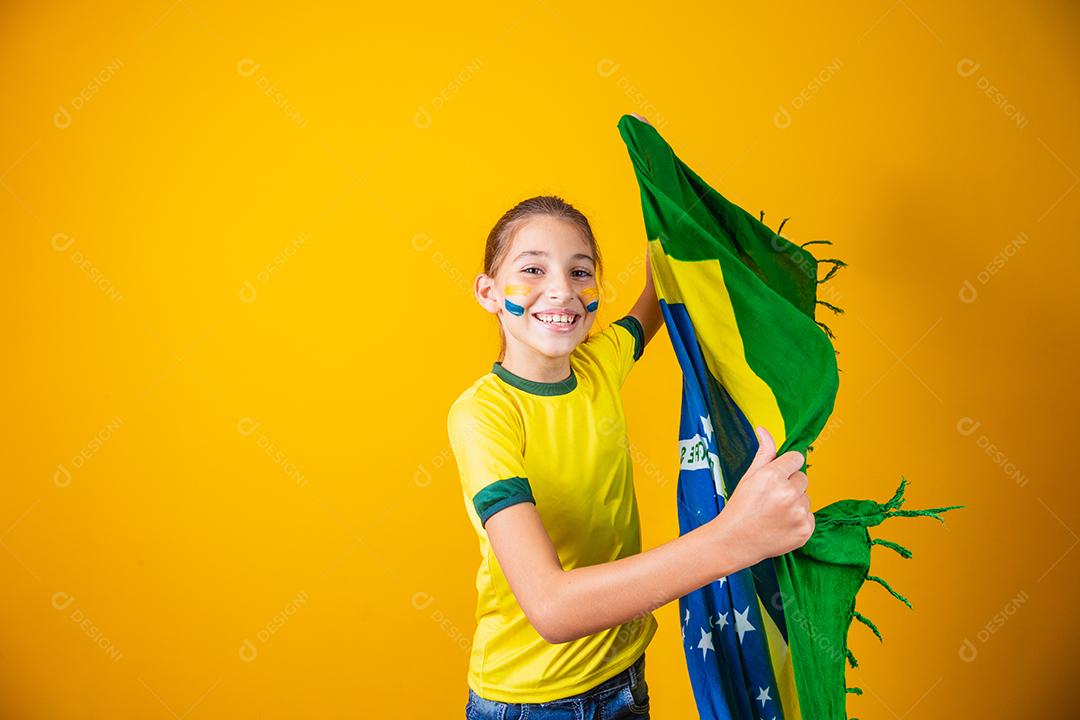 pequena garota caucasiana com bandeira do brasil em fundo amarelo. apoiador de criança brasileira