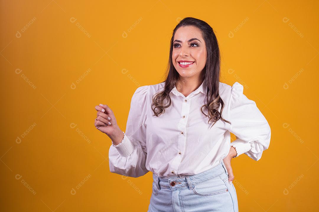 jovem morena com os braços cruzados, olhando para a câmera no fundo amarelo, com espaço livre para texto. Horizontal