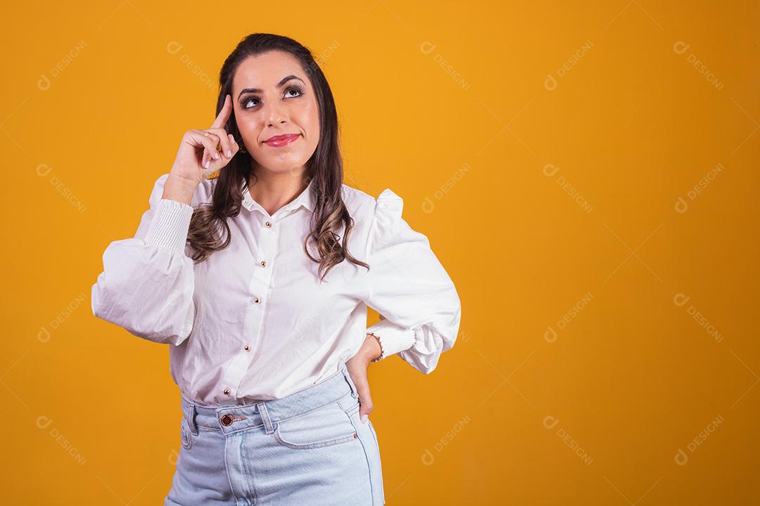 Mulher jovem e bonita de pé sobre fundo amarelo pensando em questão, expressão pensativa