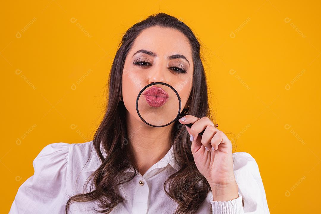 Retrato de jovem segurando lupa aos lábios, olhando para a câmera, faz gesto de beijo.