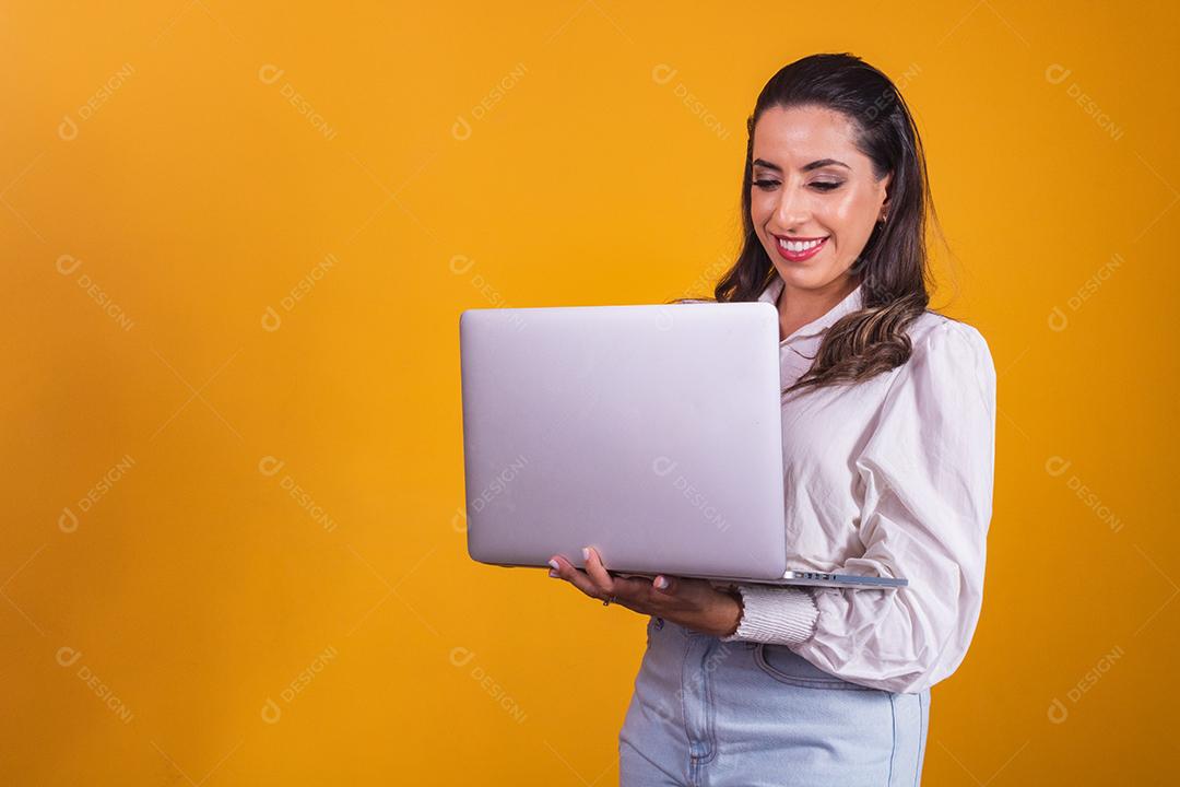 Retrato de uma linda garota segurando um laptop nas mãos dela. Escritório em casa jovem em fundo amarelo trabalhando virtual com computador.