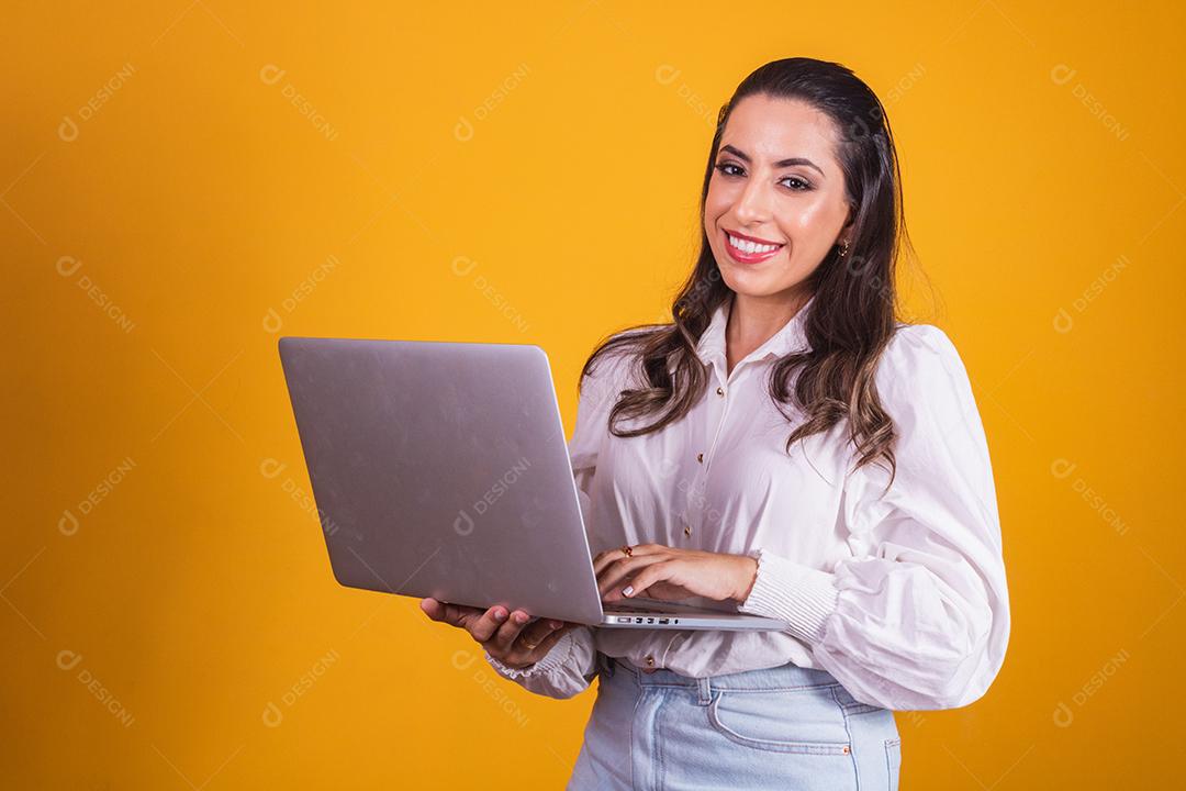 Retrato de uma linda garota segurando um laptop nas mãos dela. Escritório em casa jovem em fundo amarelo trabalhando virtual com computador.