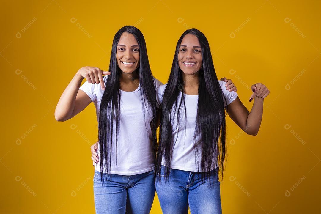 irmãs gêmeas idênticas apontando para baixo com camiseta branca