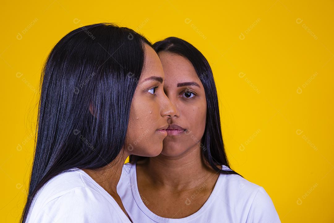 irmãs gêmeas idênticas em fundo amarelo mostrando metade do rosto um do outro. conceito de publicidade de gêmeos