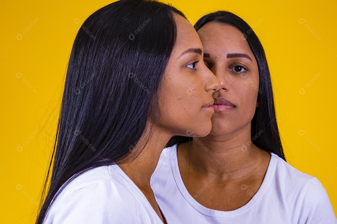 irmãs gêmeas idênticas em fundo amarelo mostrando metade do rosto um do outro. conceito de publicidade de gêmeos