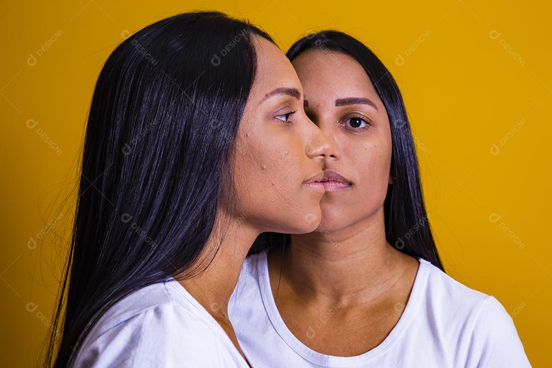 irmãs gêmeas idênticas em fundo amarelo mostrando metade do rosto um do outro. conceito de publicidade de gêmeos