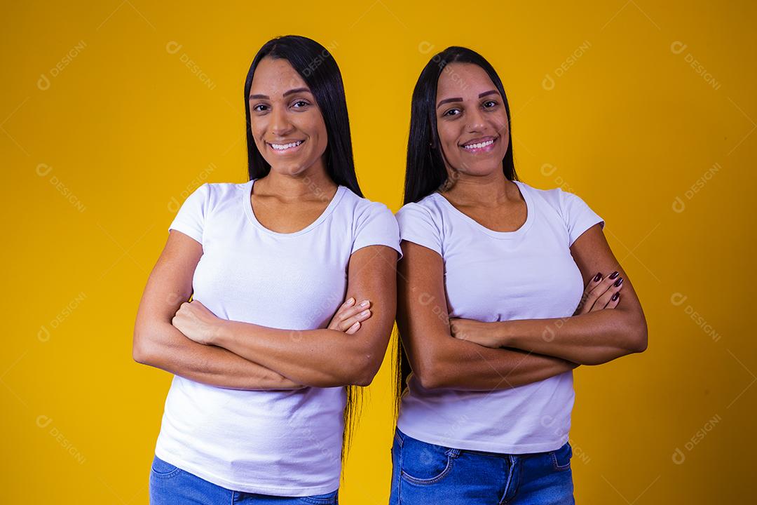 irmãs gêmeas idênticas em fundo amarelo com os braços cruzados